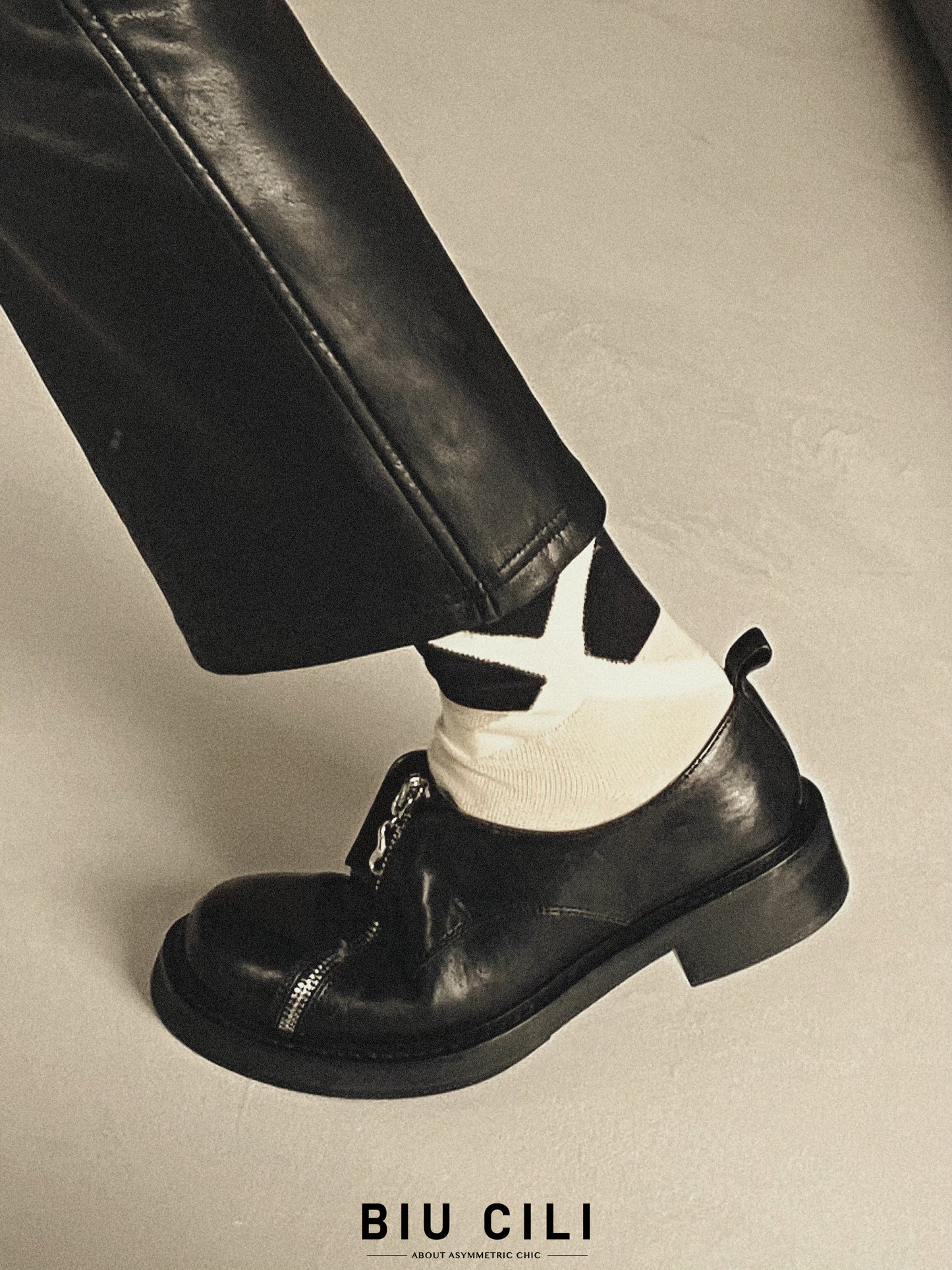 Black asymmetric leather loafers with curved zipper detail and rounded toe