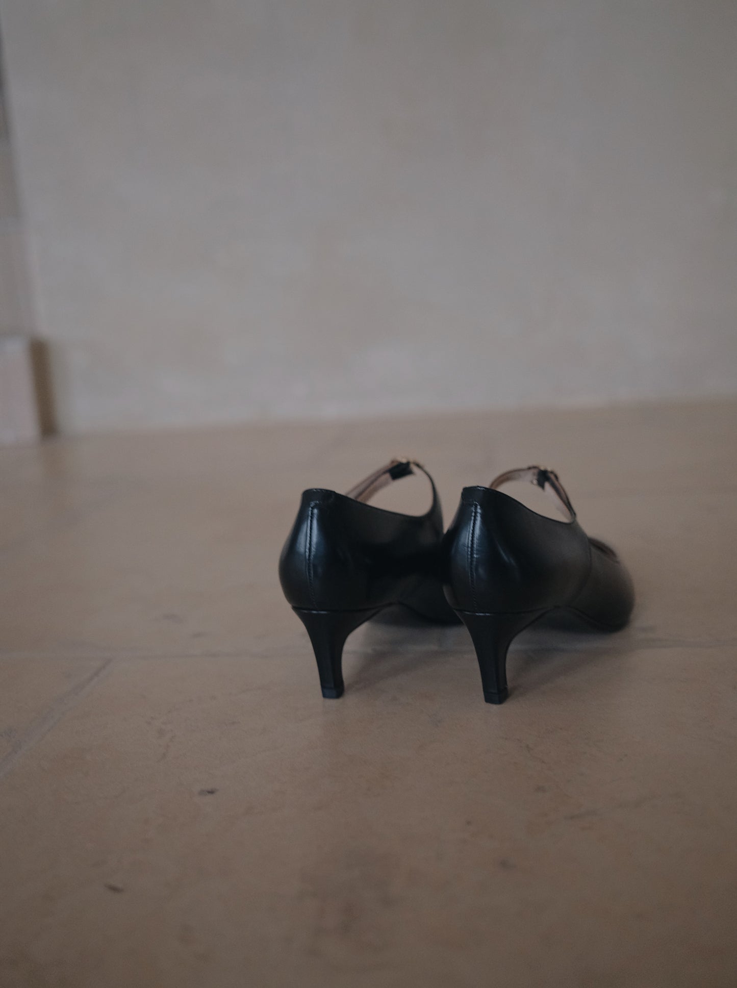 Back view of a pair of black pointed-toe leather Mary Jane heel with metal buckle, showing the mid height heels