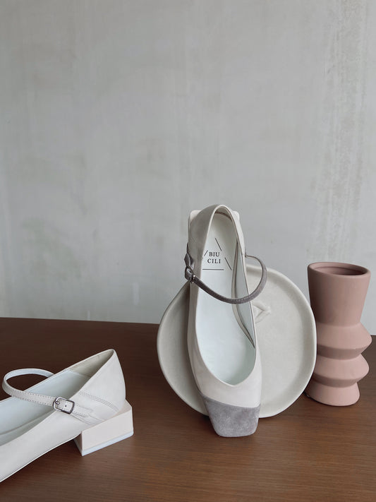 White and grey square-toe Mary Jane heels with ankle straps, styled with sculptural ceramic vases on a brown tabletop