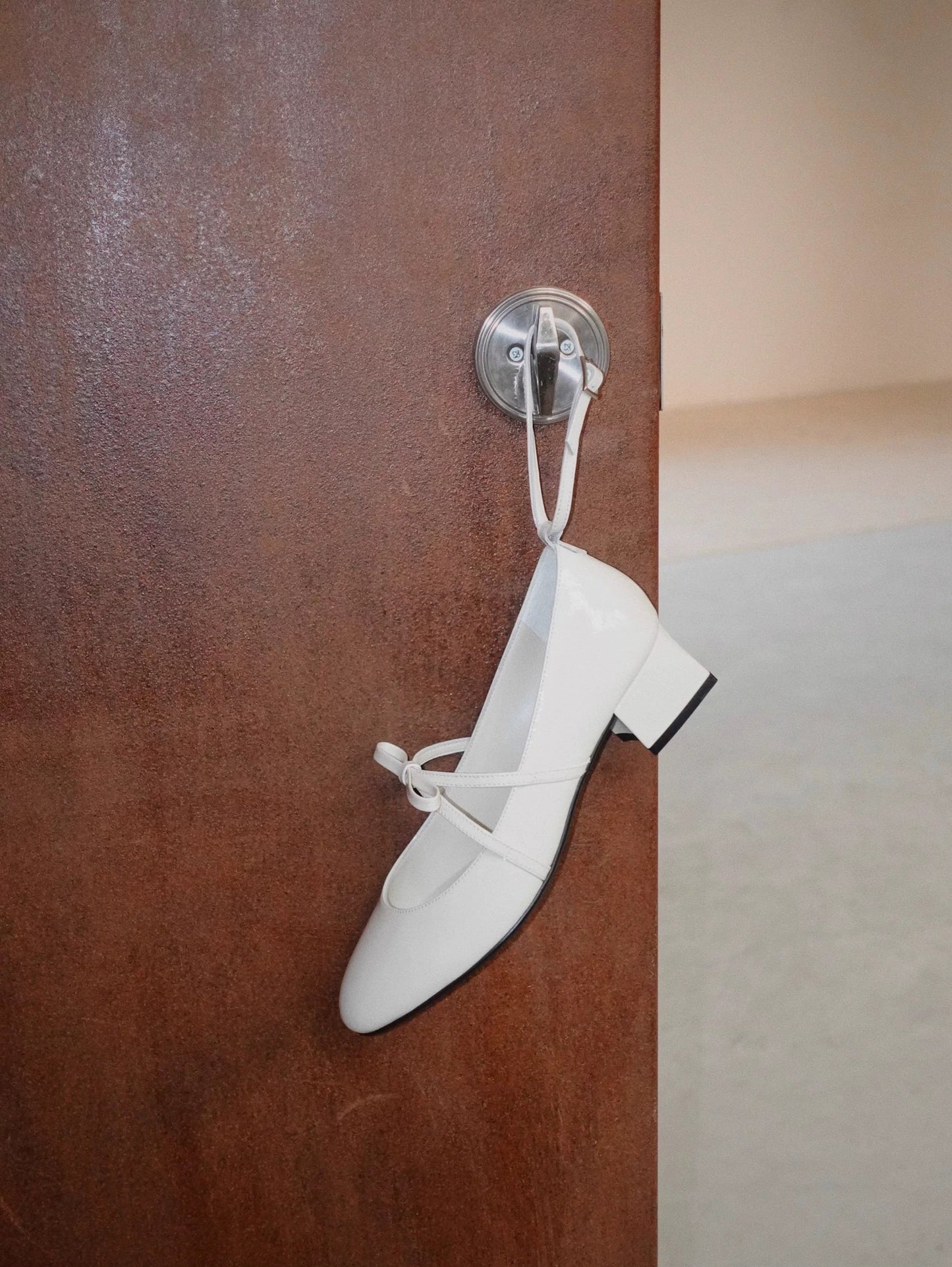 White patent leather Mary Jane heels with asymmetric bow straps, hanging on the door handle