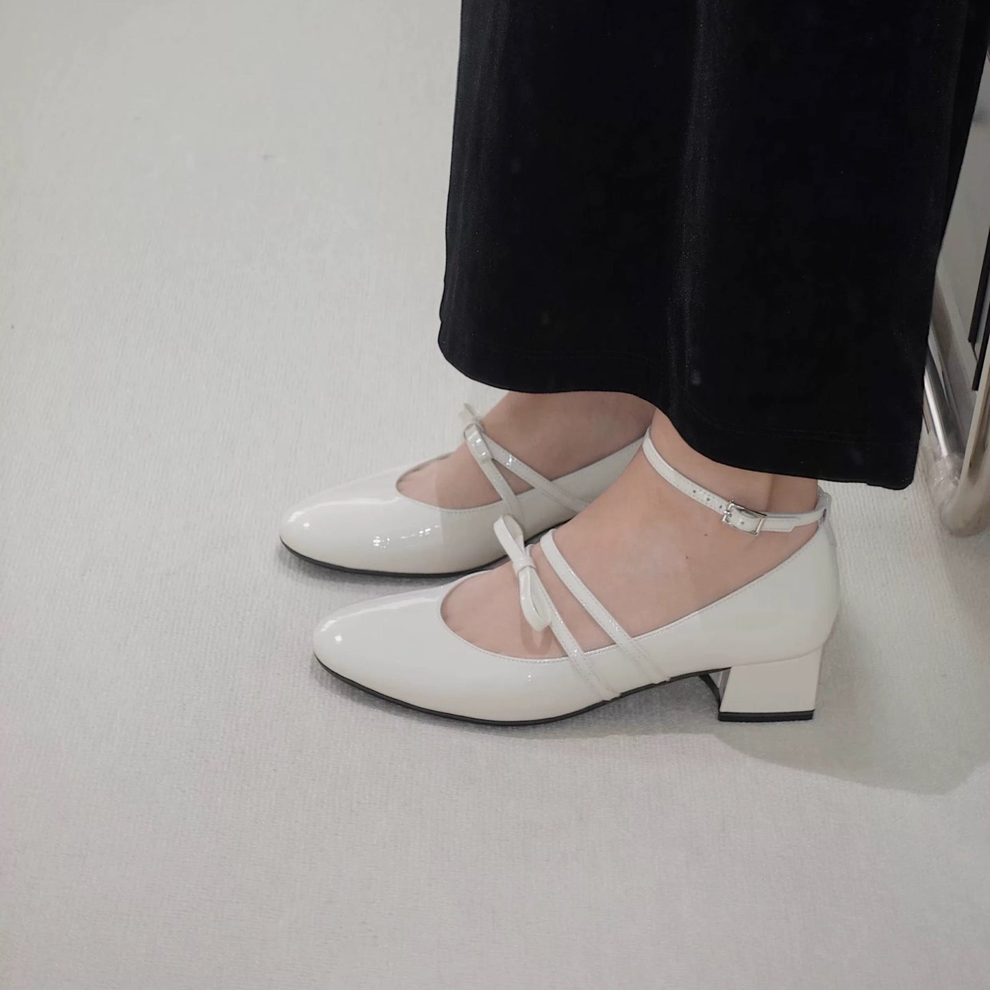 Women wearing a pair of white patent leather Mary Jane heels with asymmetric bow straps