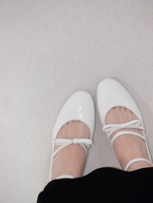 Women wearing a pair of white patent leather Mary Jane heels with asymmetric bow straps