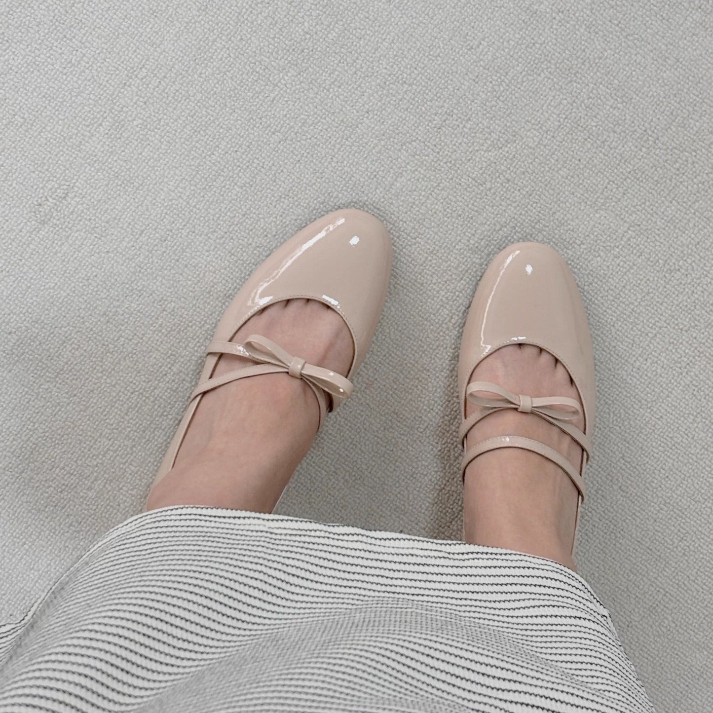 Women wearing a pair of pale pink patent leather Mary Jane heels with asymmetric bow straps