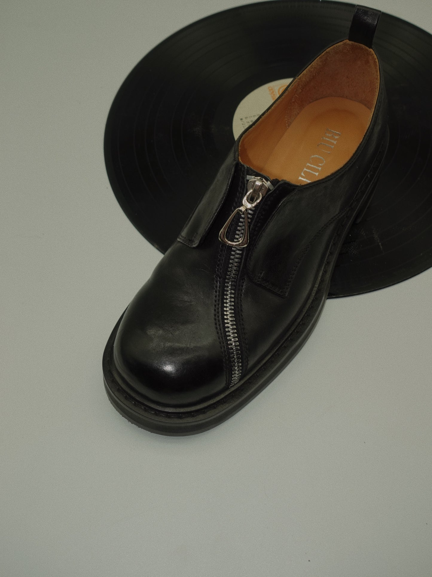 Black asymmetric leather loafers with curved zipper detail and rounded toe