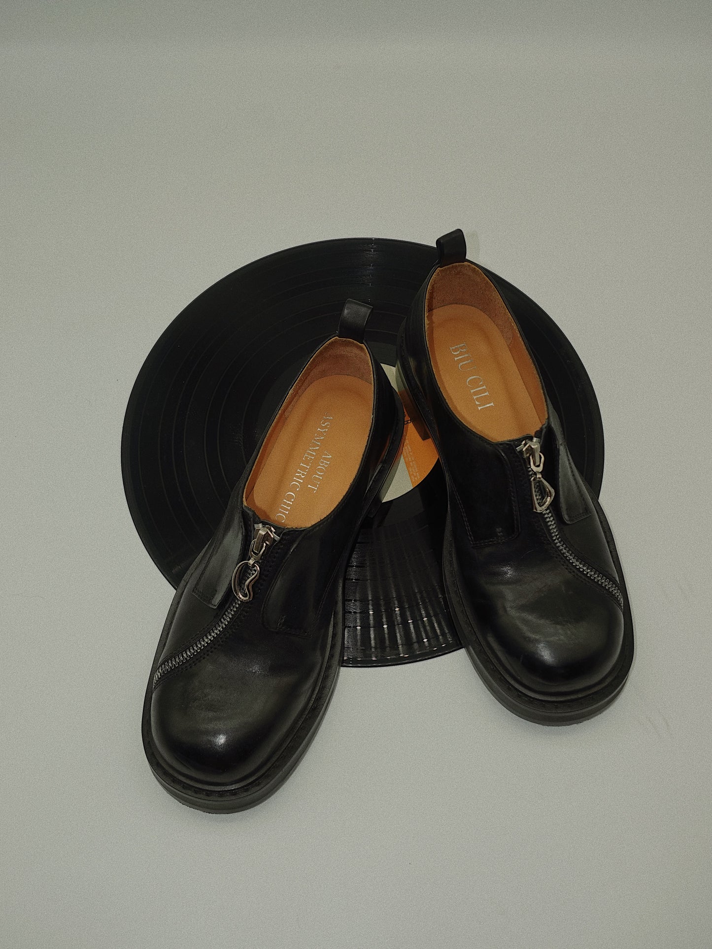 Black asymmetric leather loafers with curved zipper detail and rounded toe