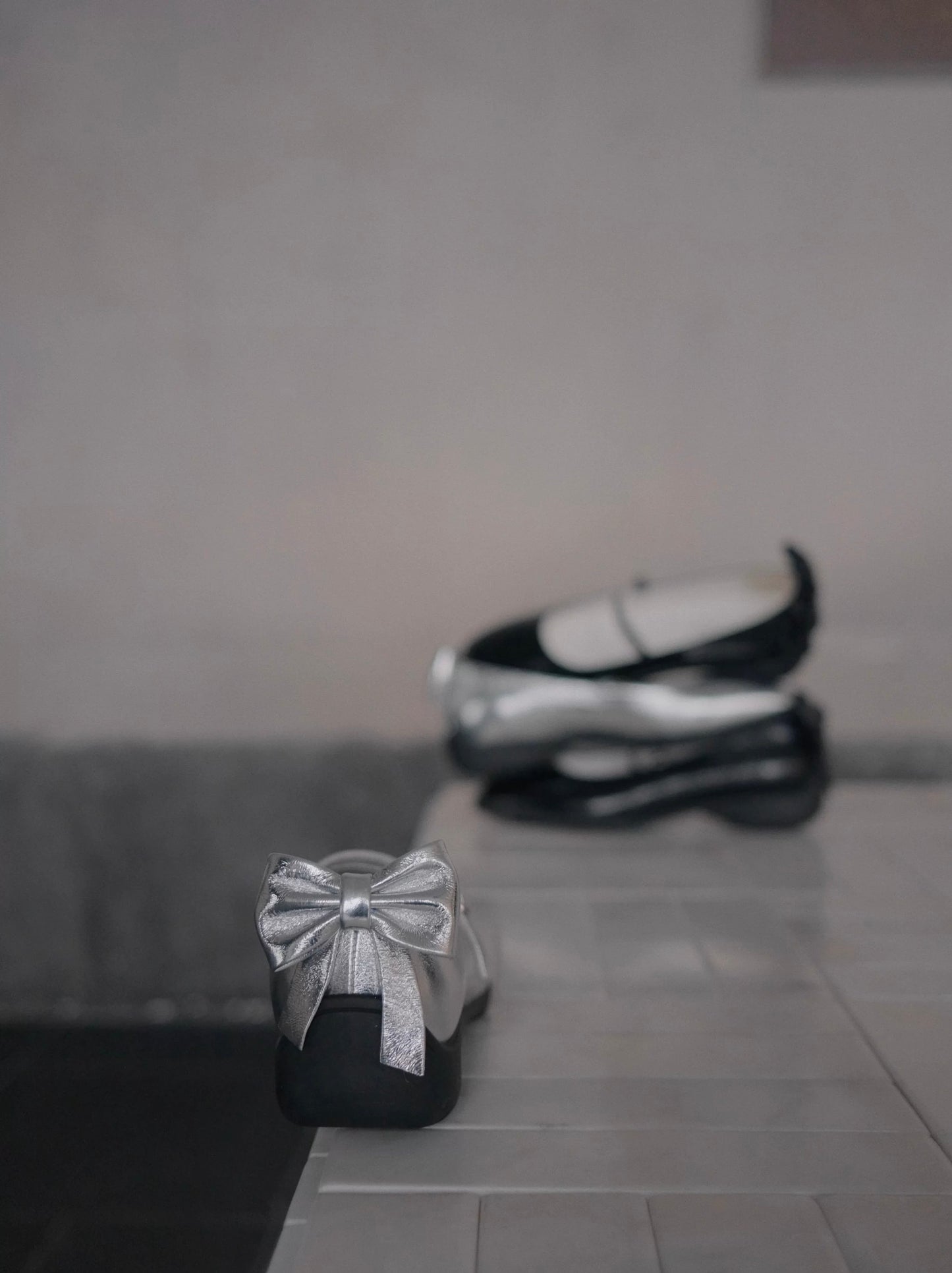 Showing three mary jane shoes stacked vertically in the back, and the back bow detail of the silver mary jane flats in the front