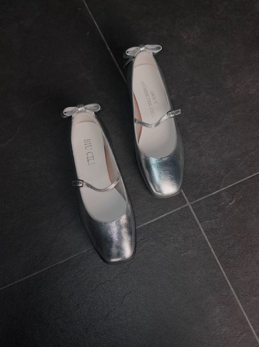 Sporty Mary Jane shoes in shimmering silver with back bow place on a dark rought floor - top view