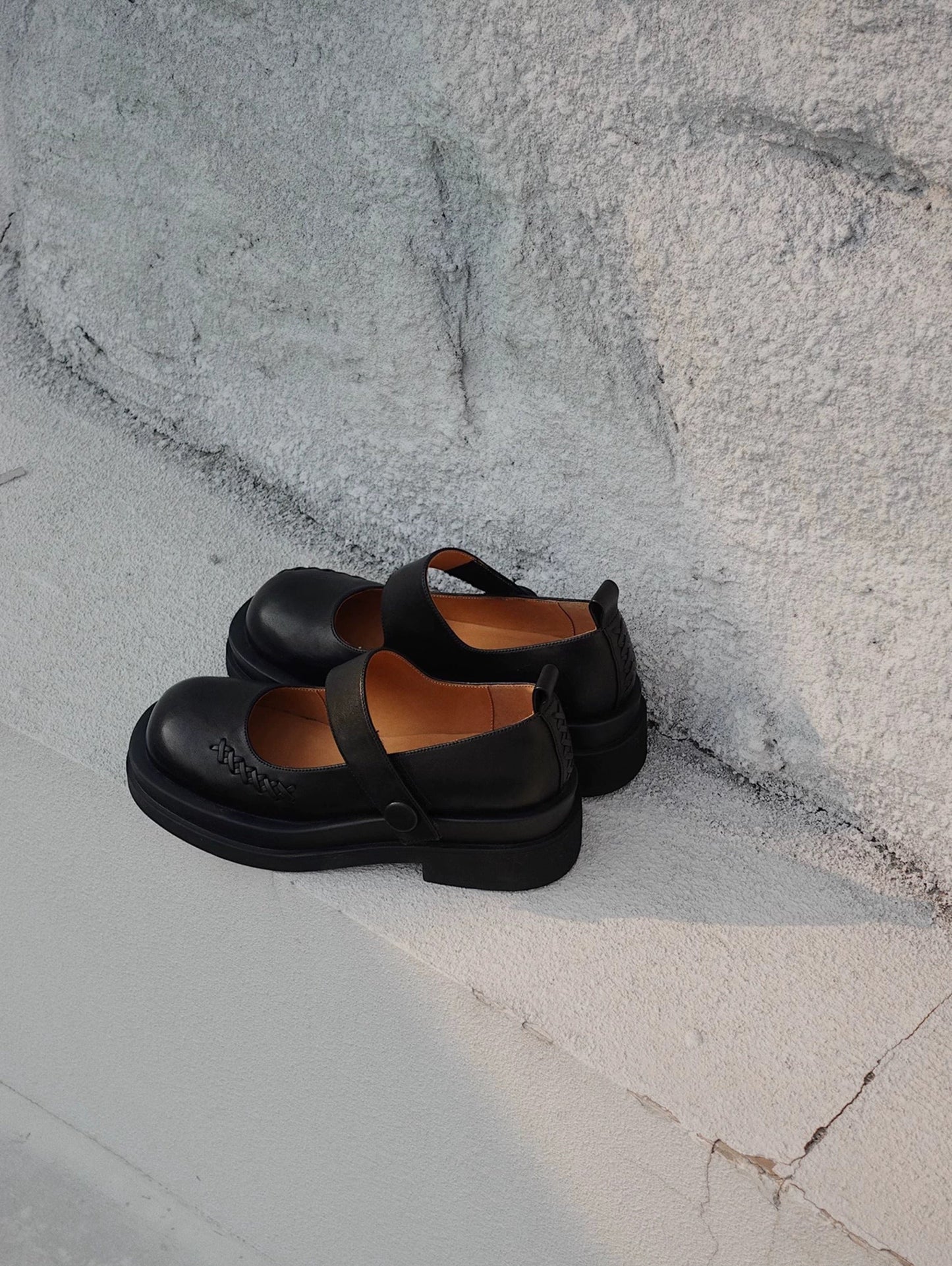 Black platform Mary Jane shoes with wide strap and low block heel, displayed on a textured concrete floor beside a wall