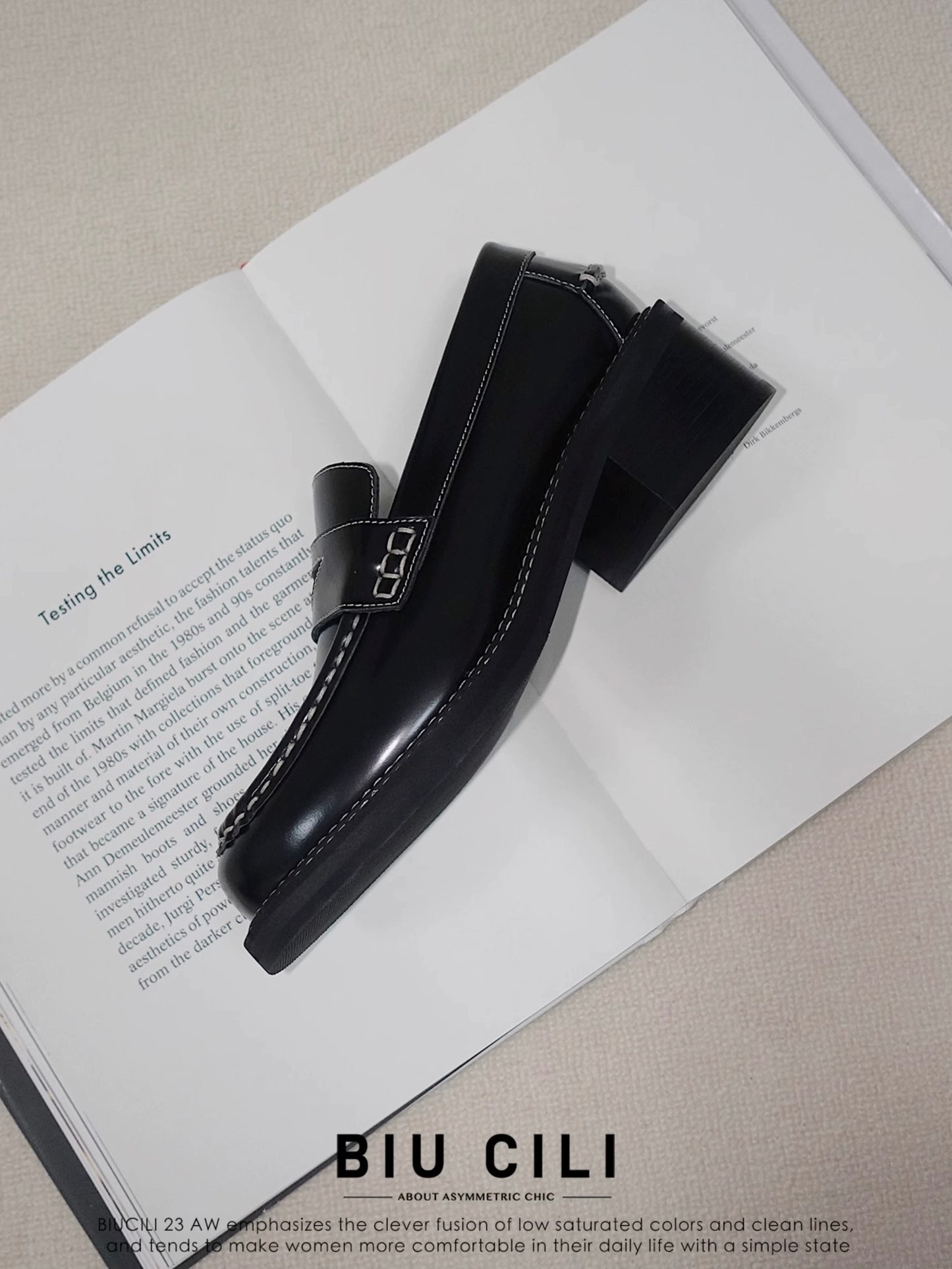 Side view of a black leather loafer heels with asymmetric details for women, placing on an open book
