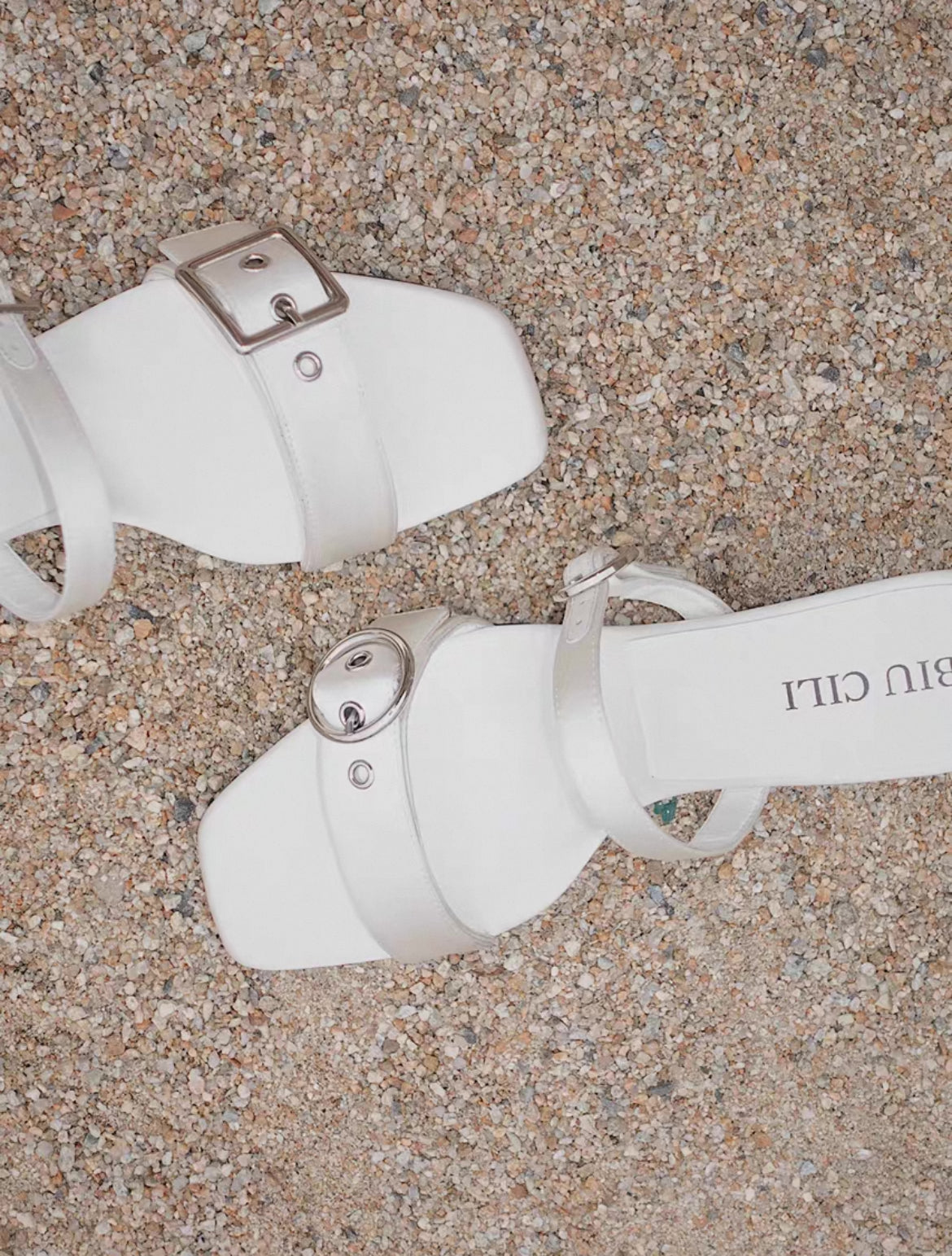 A pair of mid heel sandal with two thick white silk straps and shiny asymmetrical silver buckle - top view