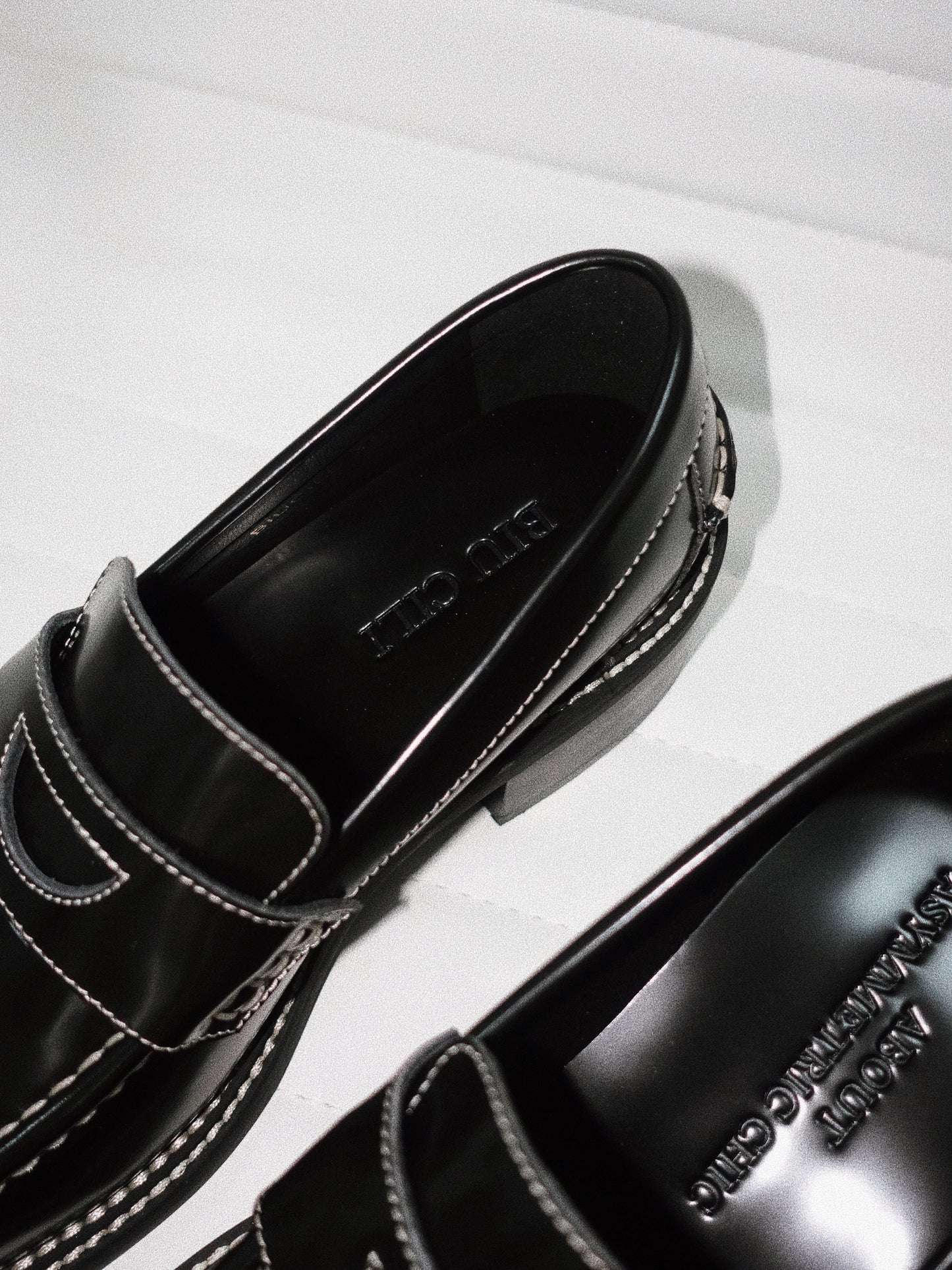 A close view of the back off-white stitching details of a pair of black leather loafer heels with asymmetric details for women