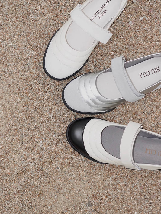 Close-up of three BIU CILI Mary Jane flats in white, silver, and black toe cap styles, displayed on textured gravel surface