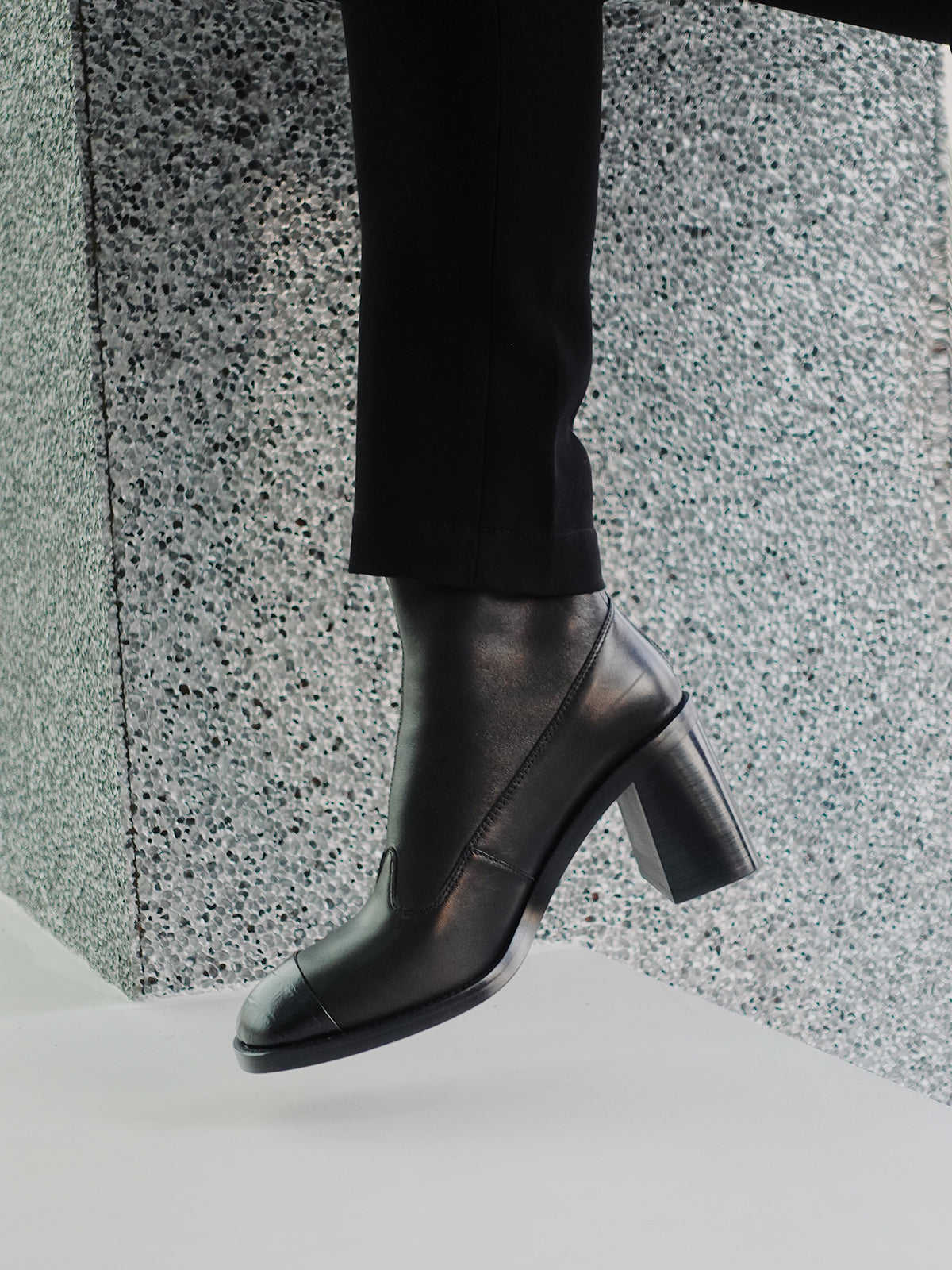 A woman wearing a pair of women's black leather square-toe ankle boots with block heels