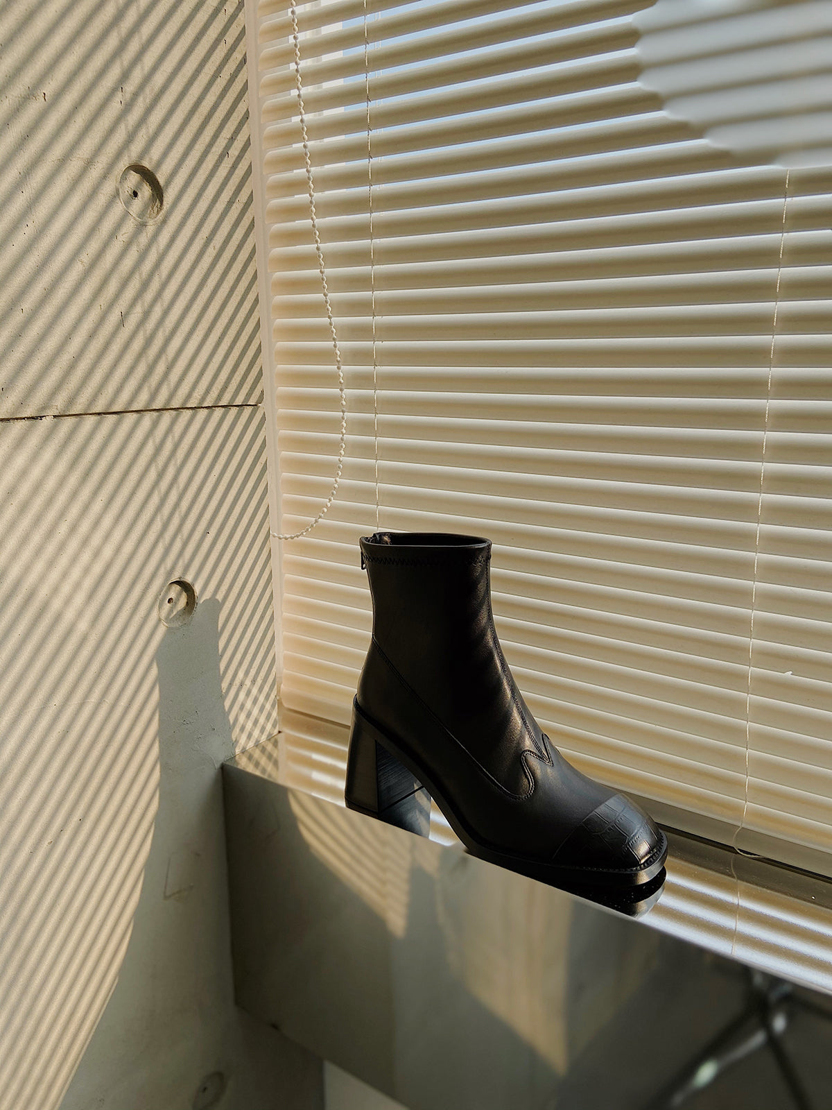 Women's black leather square-toe ankle boots with block heels, styled against a window in warm natural light