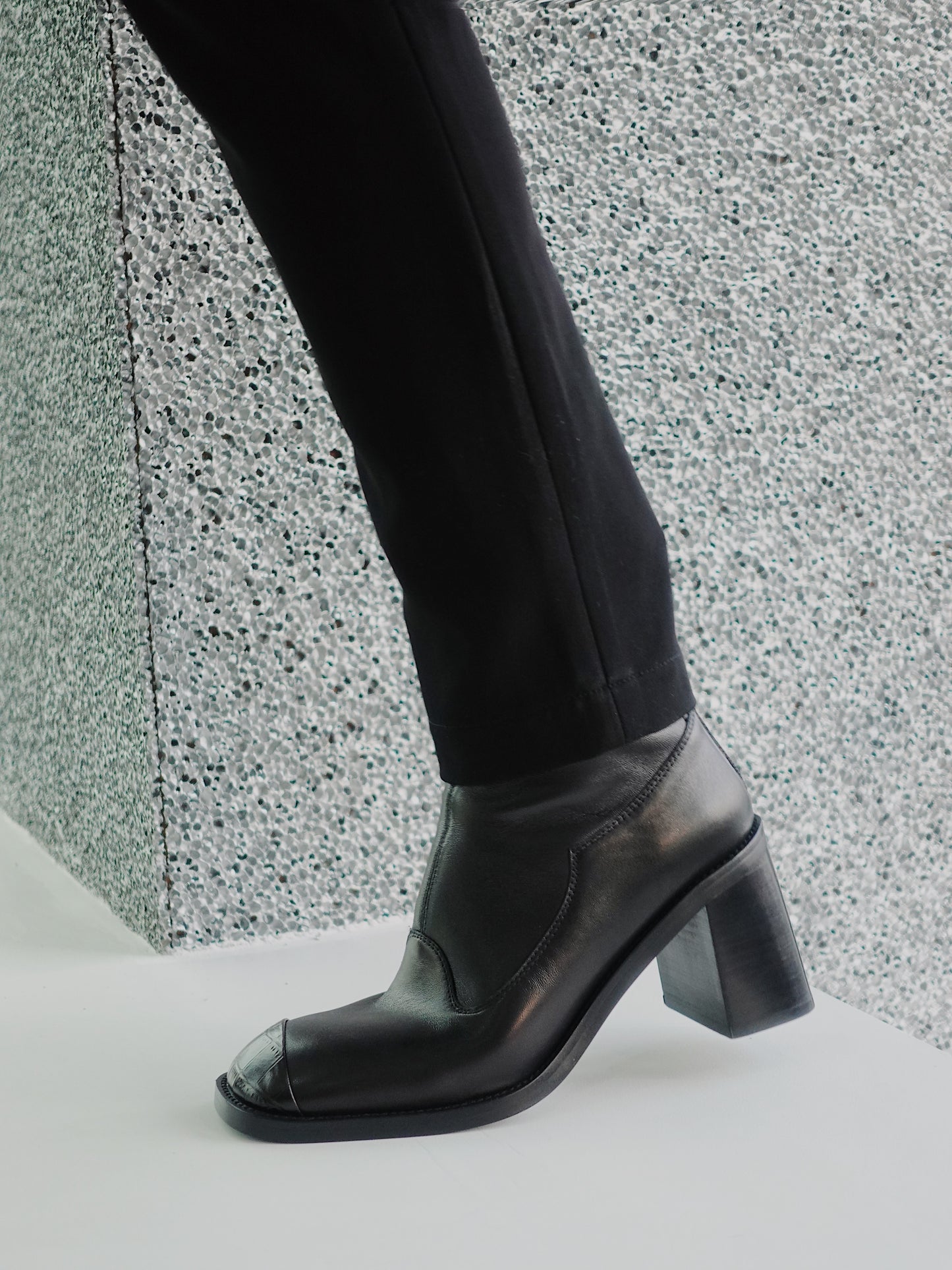 A woman wearing a pair of women's black leather square-toe ankle boots with block heels