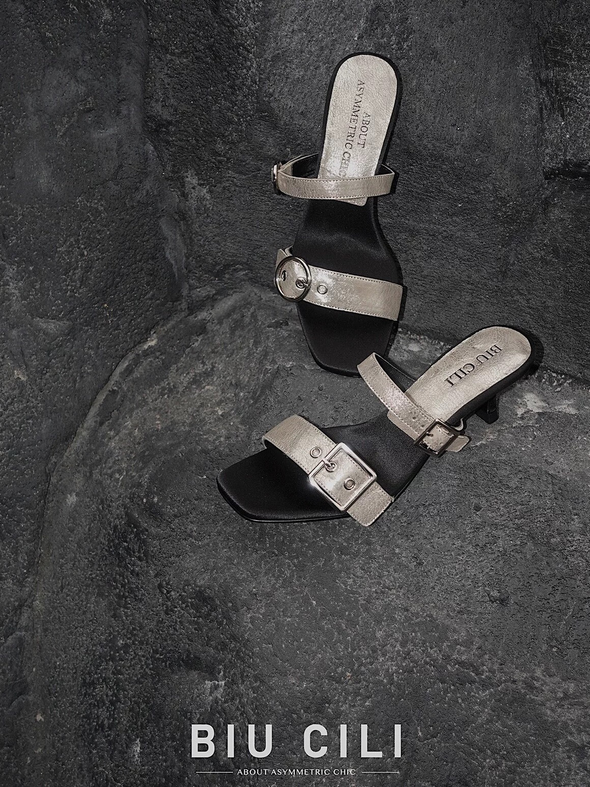 Minimalist mid heel sandals with asymmetrical silver buckle – top view - placed on a rough surface
