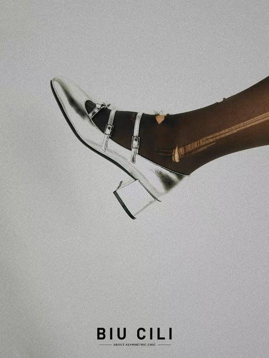 Metallic silver Mary Jane heels with triple asymmetric straps and block heel.