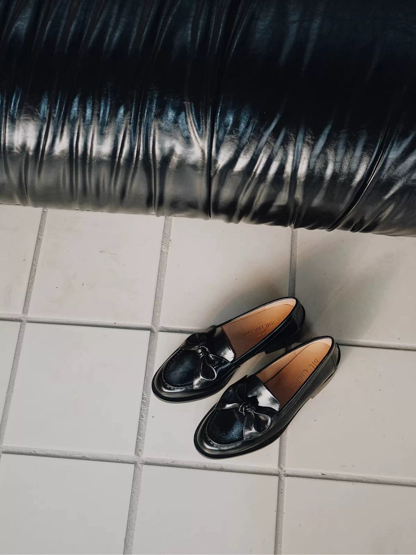 Black loafers on a tiled floor with a black pipe in the background