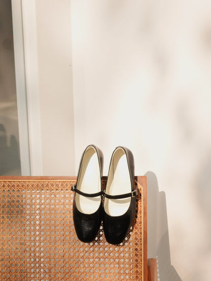 A pair of classic black mary jane flats on a neutral color chair