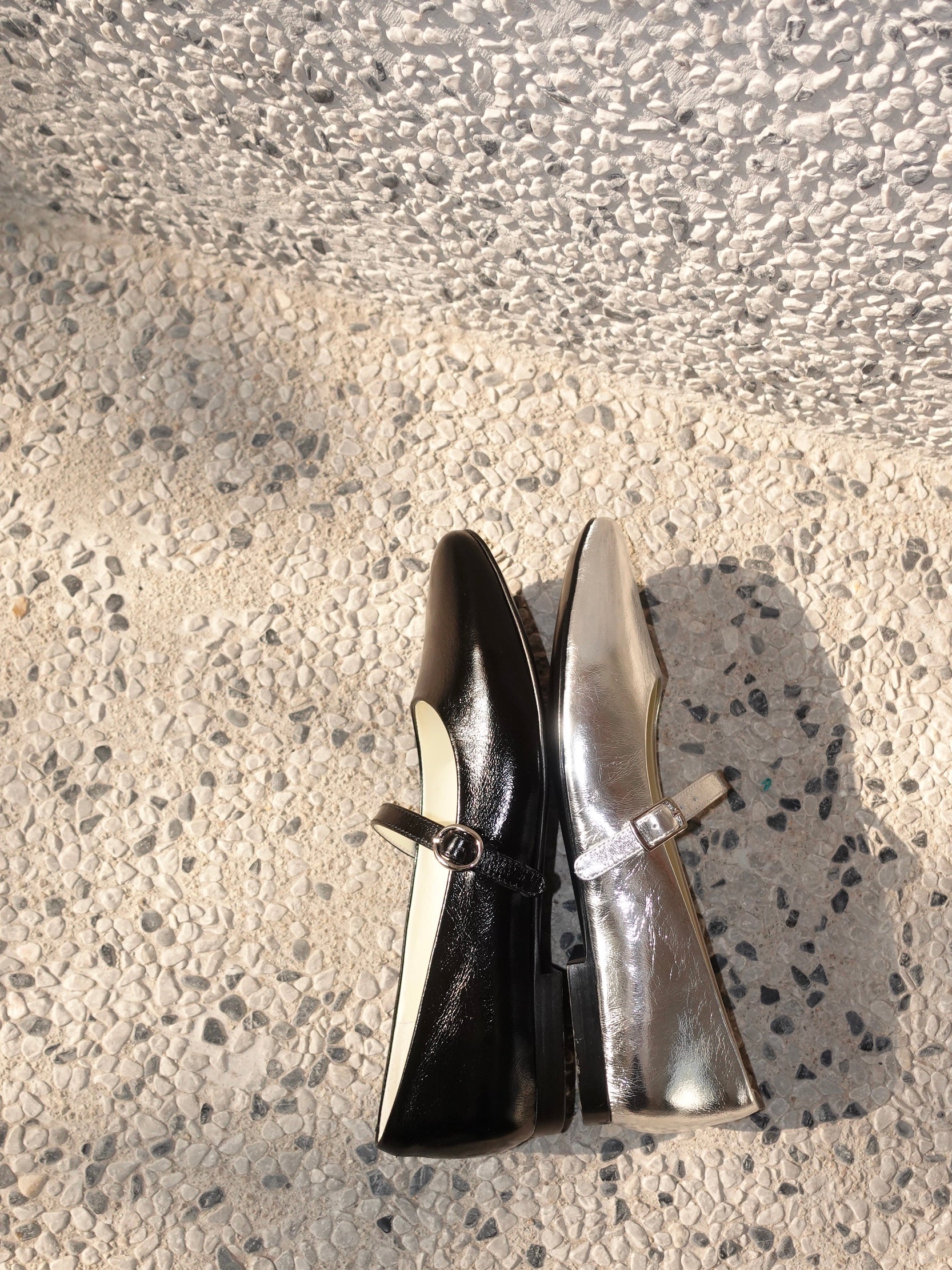 Two colors of mary jane flats shown their sideways, placing on a rough surface