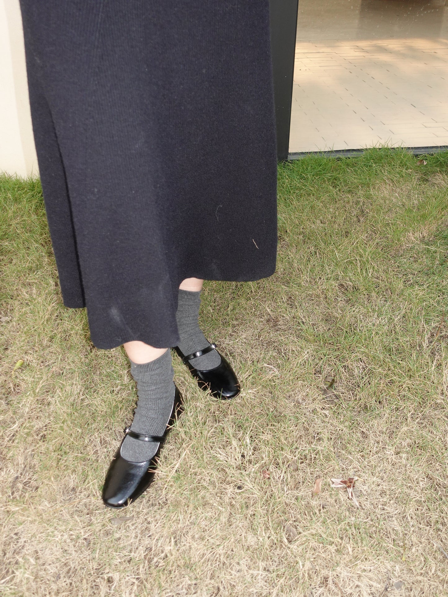 Women wearing a pair of black mary jane flats with grey socks in side, and pairing with black dress