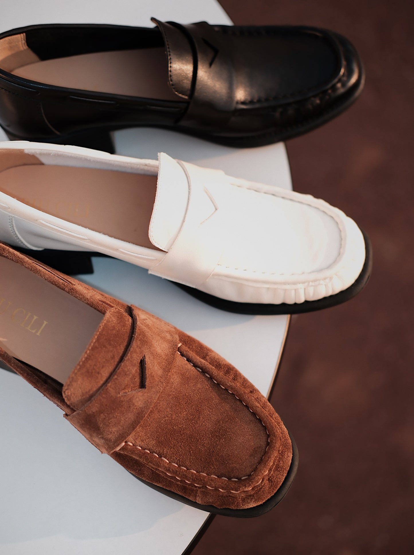Women's loafers with asymmetric detail in front on a round white table, photographed in warm natural light