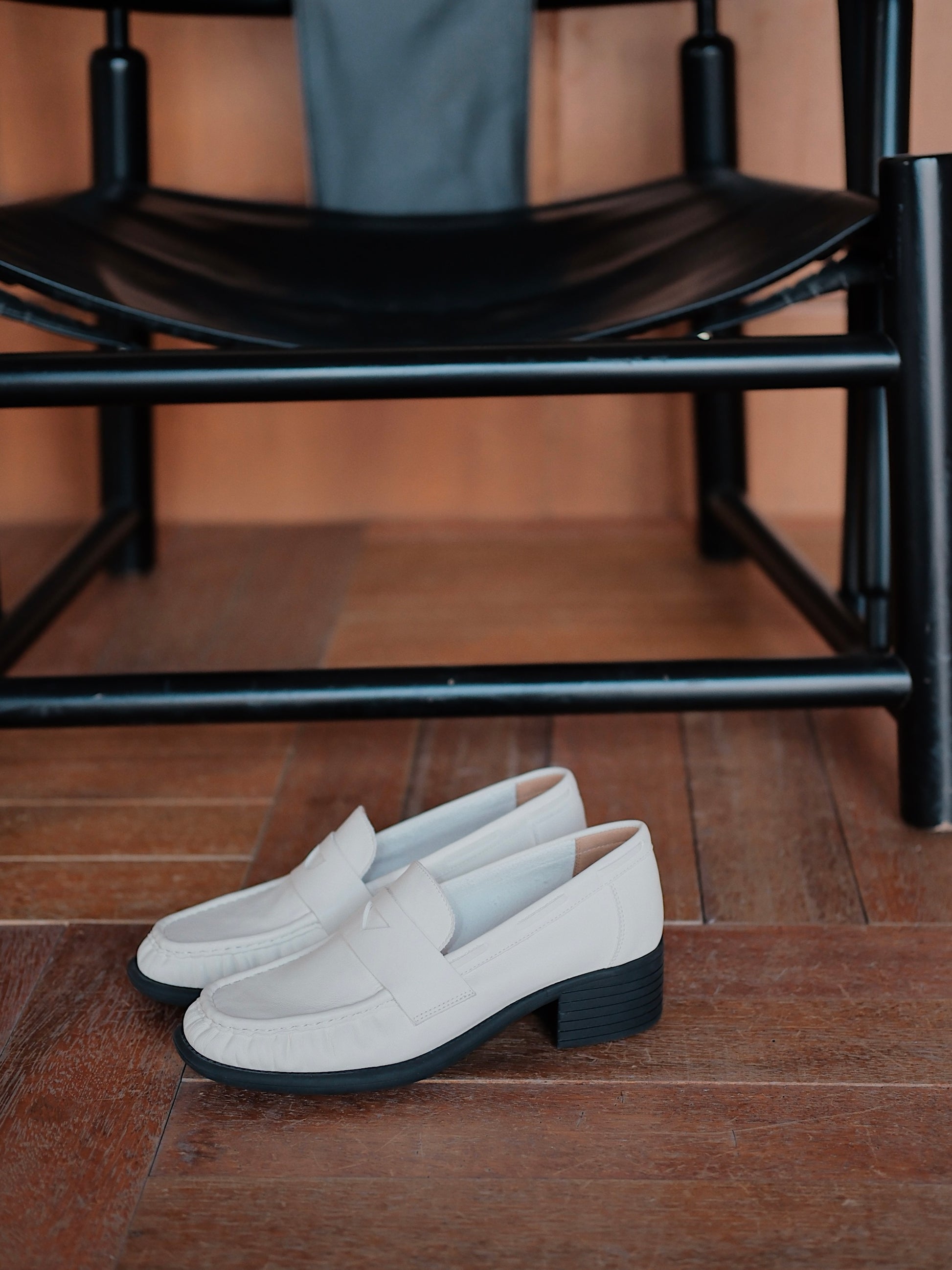 Women's white leather loafer heels with asymmetric detail, placed on the floor