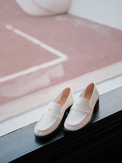 Women's white leather loafer heels with asymmetric detail besides the window