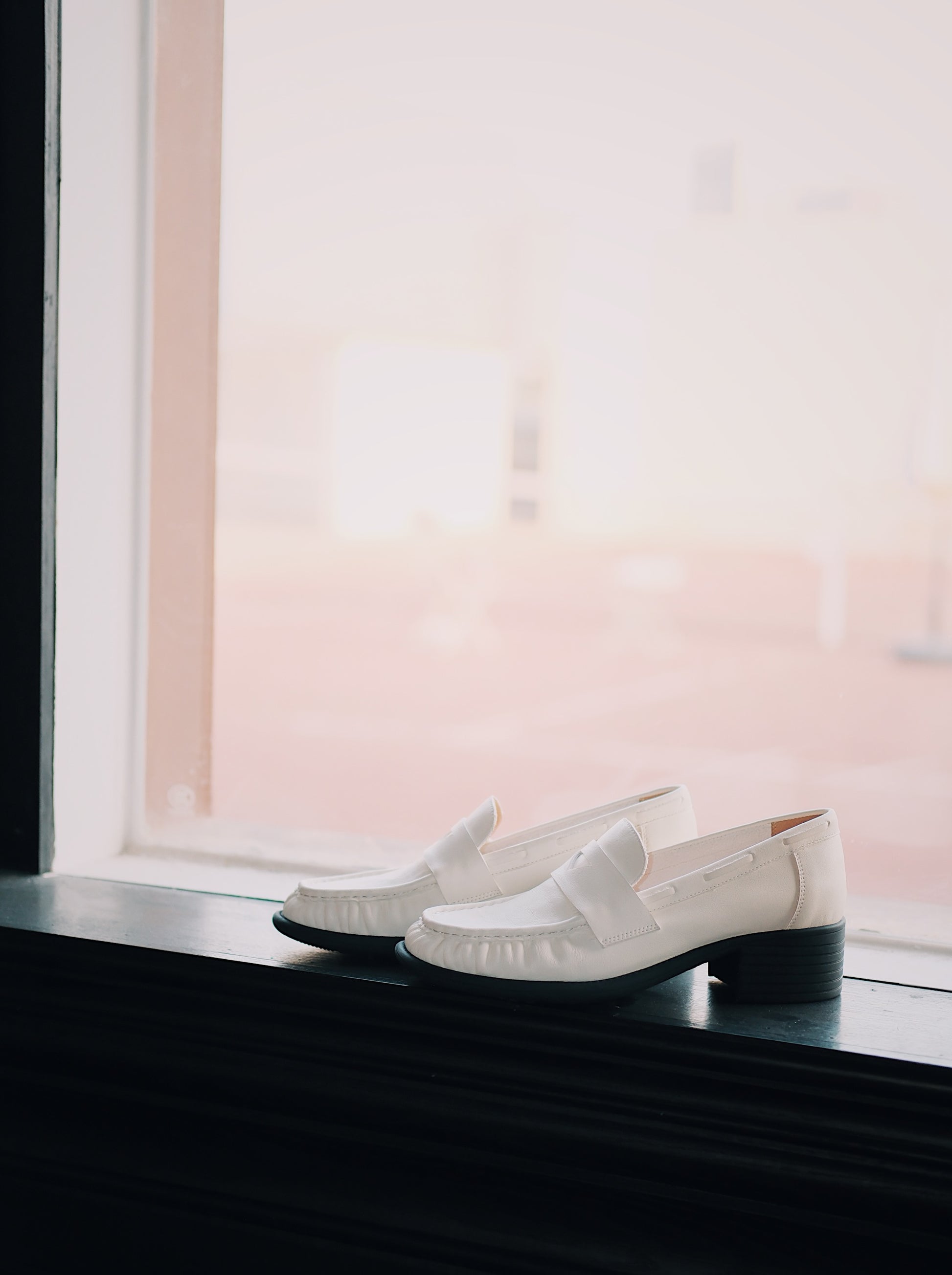 Women's white leather loafer heels with asymmetric detail besides the window