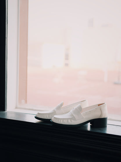 Women's white leather loafer heels with asymmetric detail besides the window