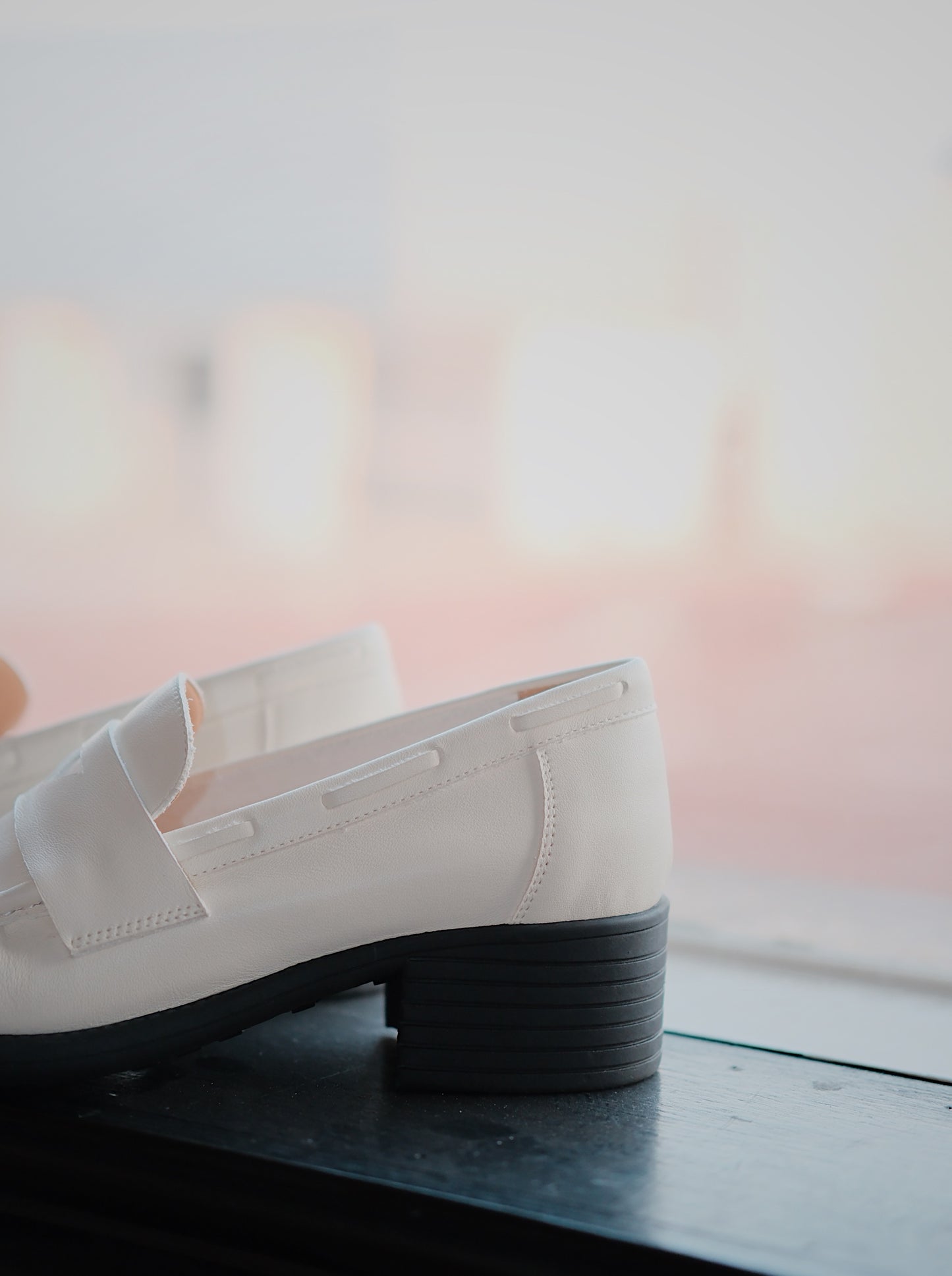 Women's white leather loafer heels with asymmetric detail besides the window