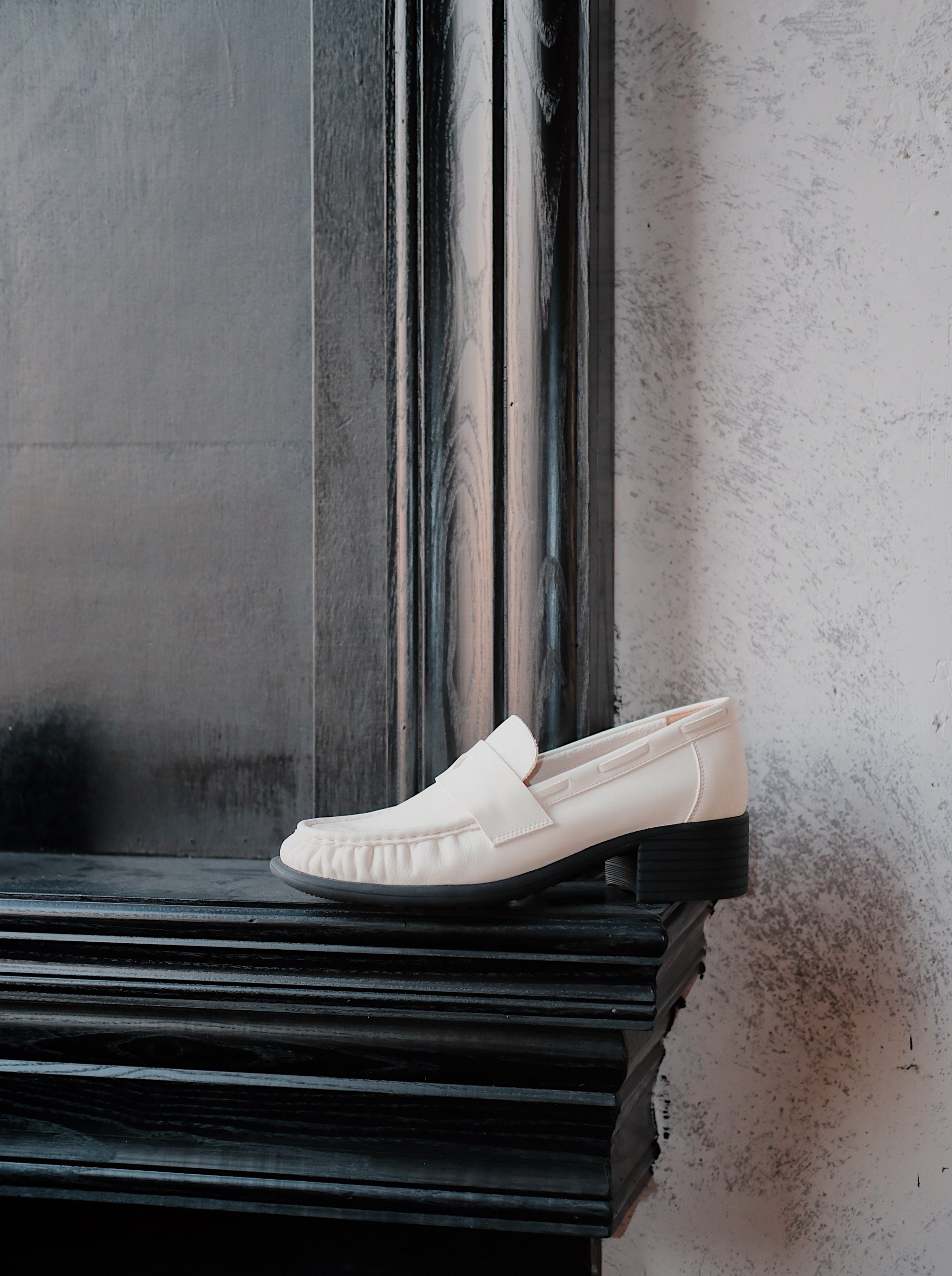 Women's white leather loafer heels with asymmetric detail on a surface