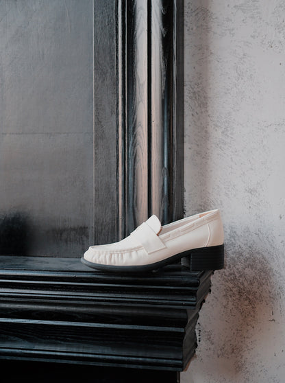 Women's white leather loafer heels with asymmetric detail on a surface