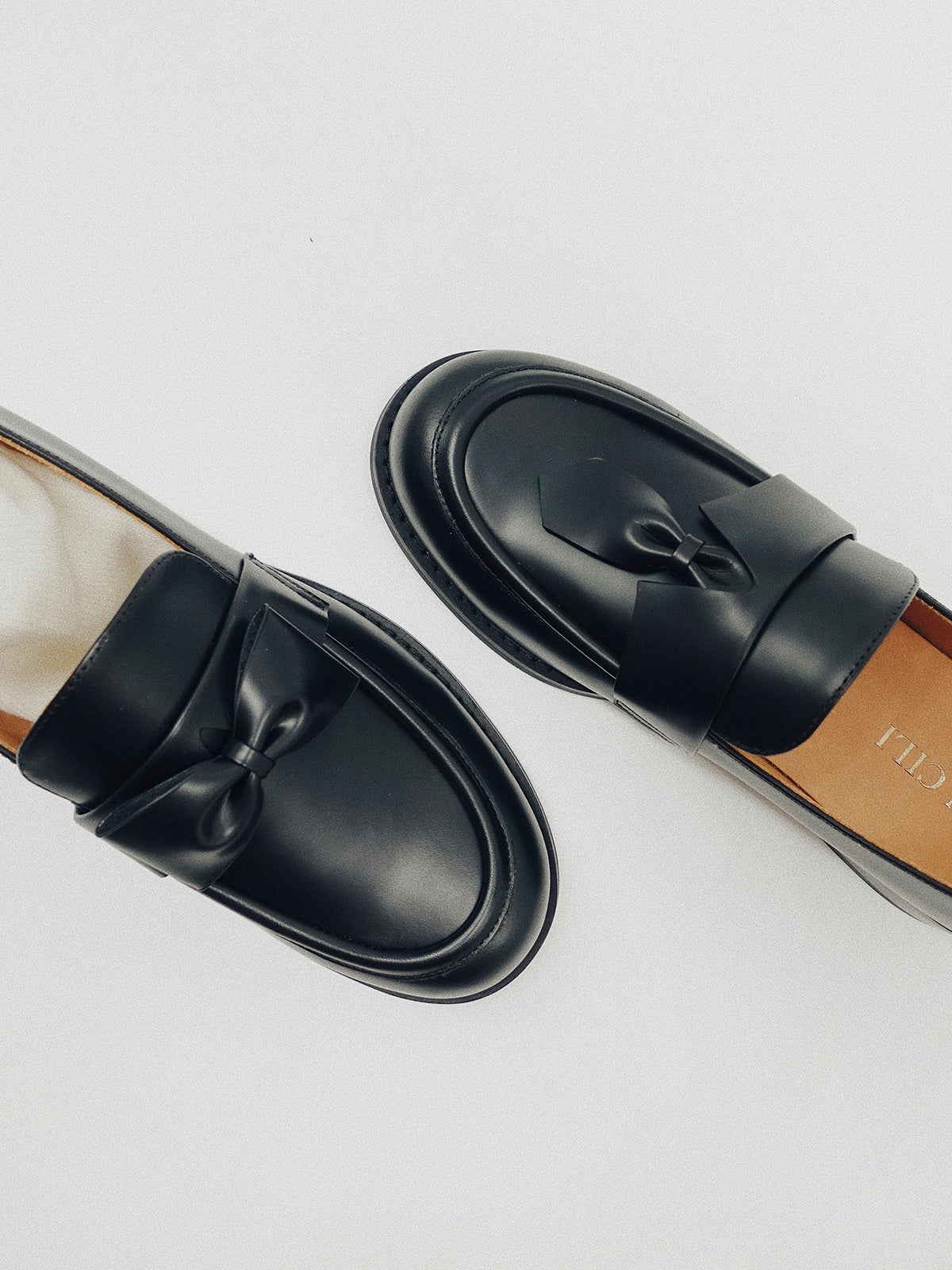 Black leather loafers for women featuring asymmetric tie and bow details, crafted in matte calfskin with low heel and soft structure, shown on white background.