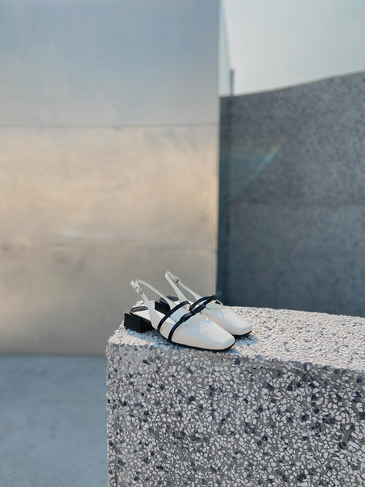 White Mary Jane shoes with square toe and black asymmetric bow straps, contrast heel, and soft leather finish.