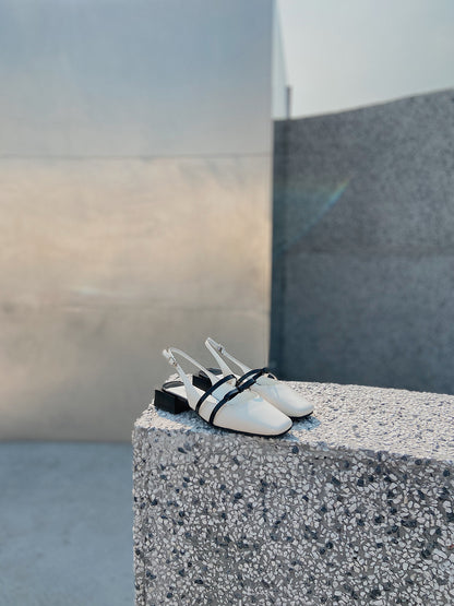 White Mary Jane shoes with square toe and black asymmetric bow straps, contrast heel, and soft leather finish.