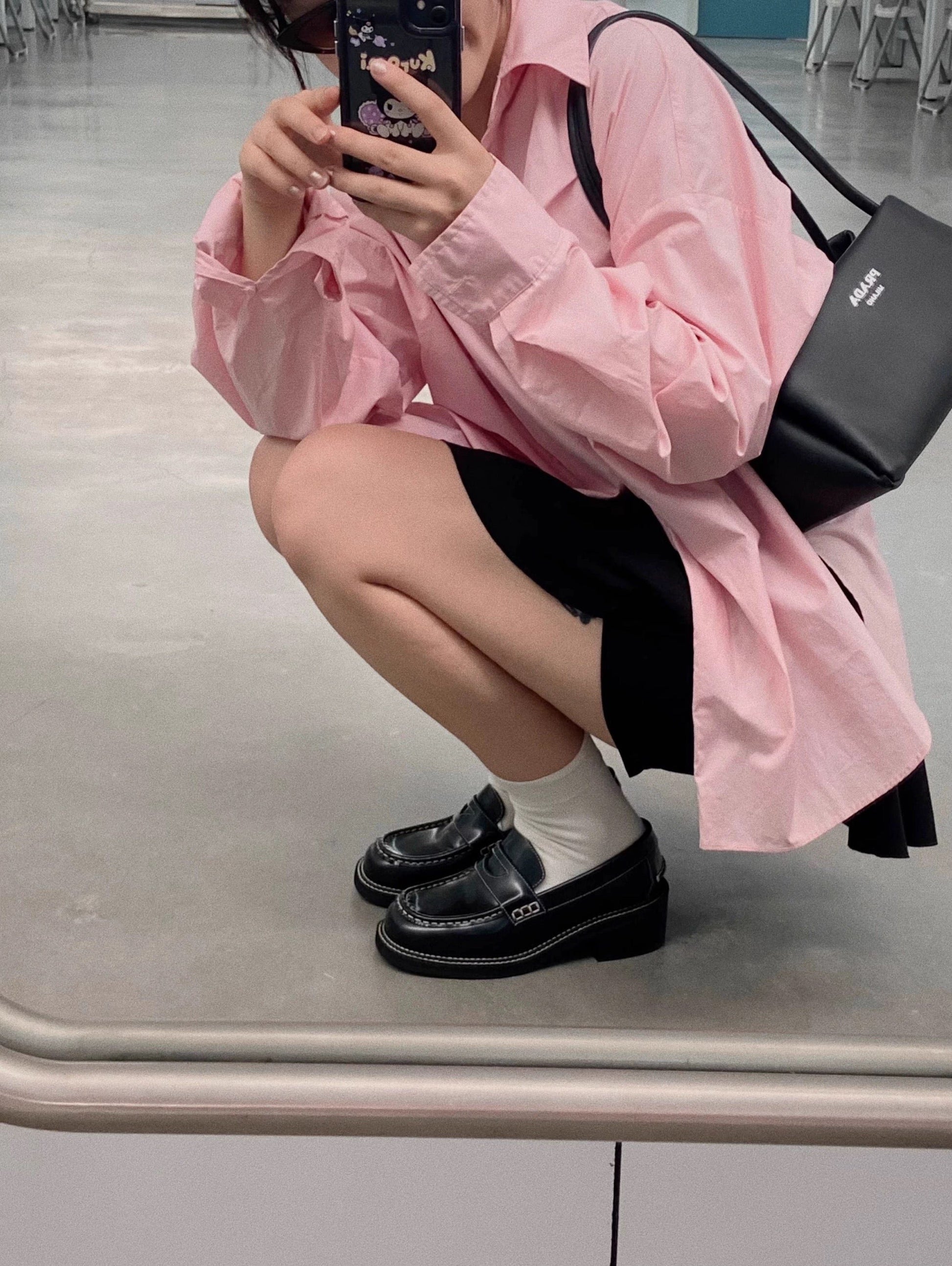 Woman wearing a pair of black leather loafer heels with white socks underneath, pairing with pink shirt top, taking the photo from the mirror