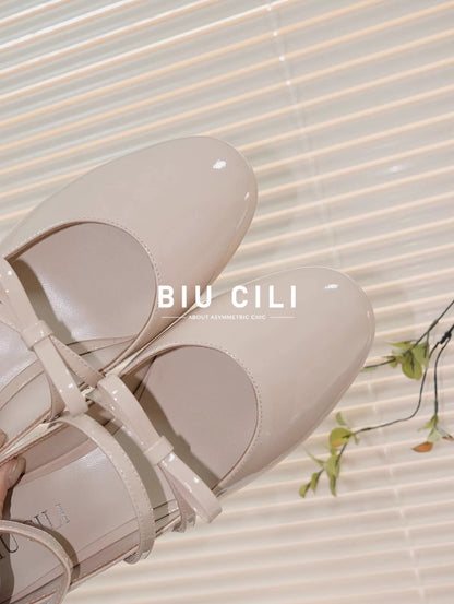Beige patent leather Mary Jane heels with asymmetric bow straps
