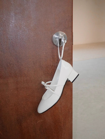 White patent leather Mary Jane heels with asymmetric bow straps, hanging on the door handle