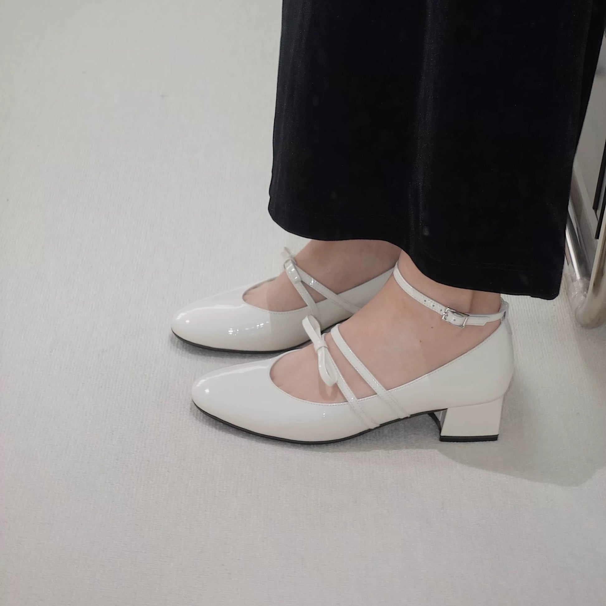 Women wearing a pair of white patent leather Mary Jane heels with asymmetric bow straps