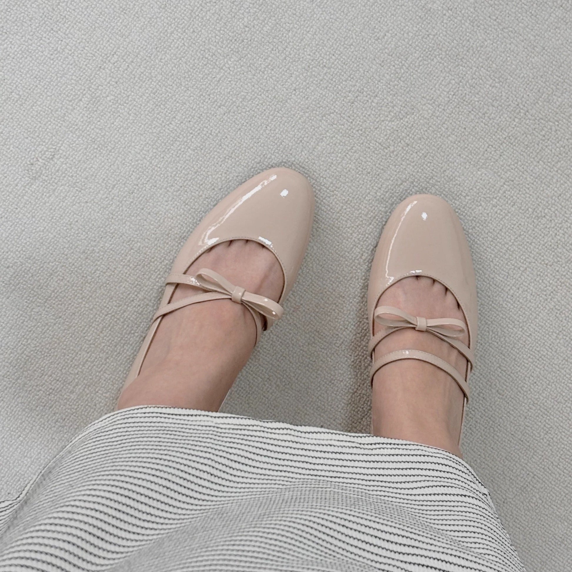 Women wearing a pair of pale pink patent leather Mary Jane heels with asymmetric bow straps