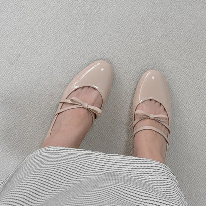 Women wearing a pair of pale pink patent leather Mary Jane heels with asymmetric bow straps