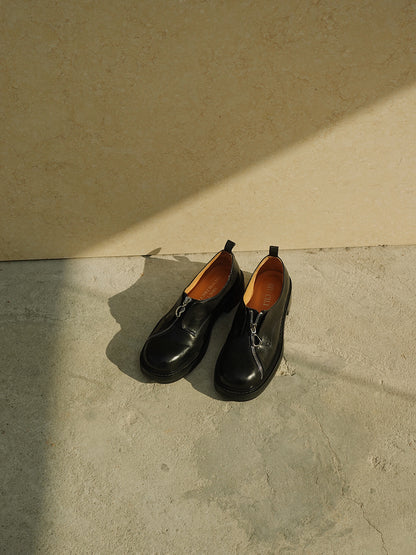 Black asymmetric leather loafers with curved zipper detail and rounded toe