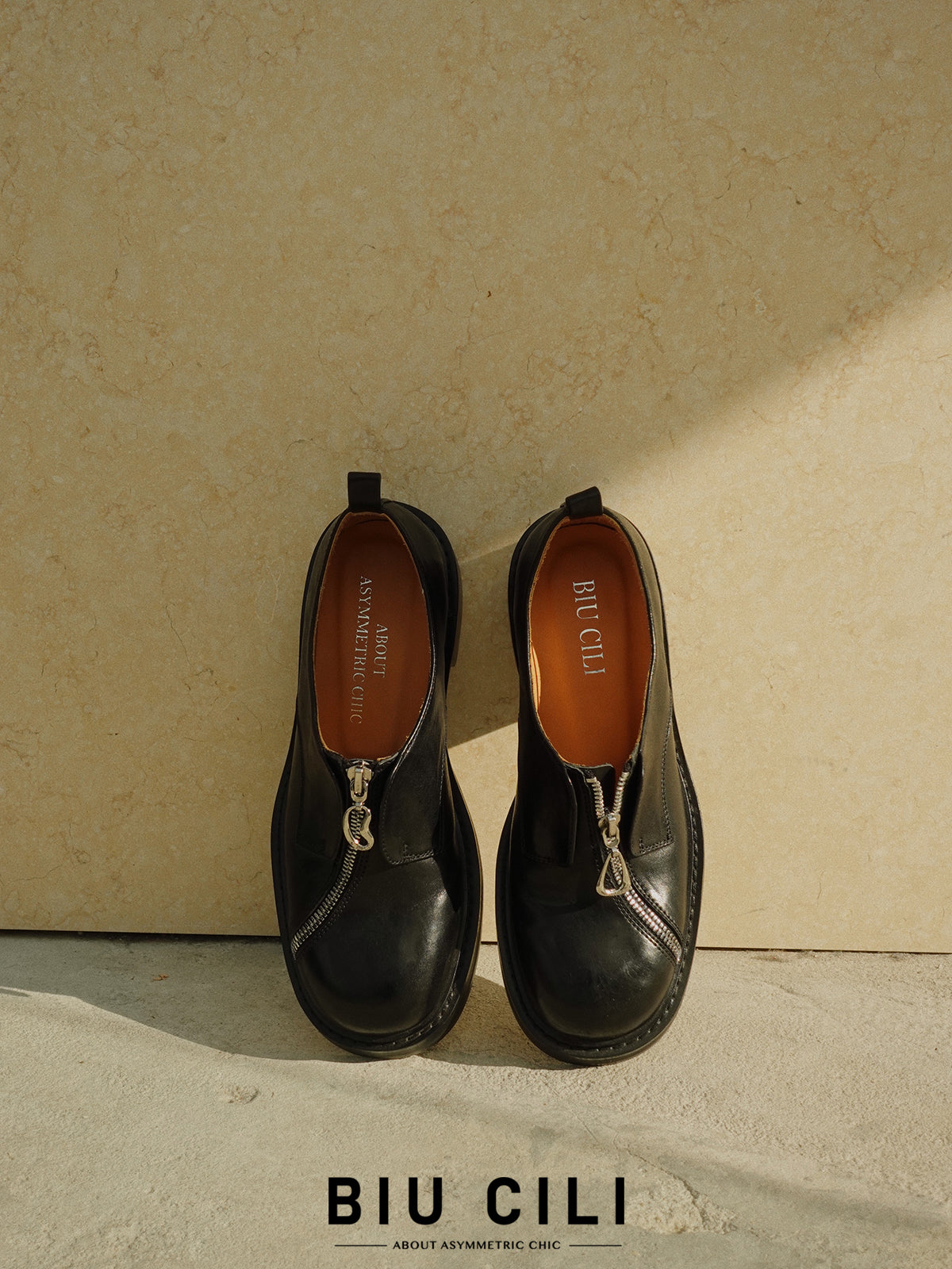 Black asymmetric leather loafers with curved zipper detail and rounded toe