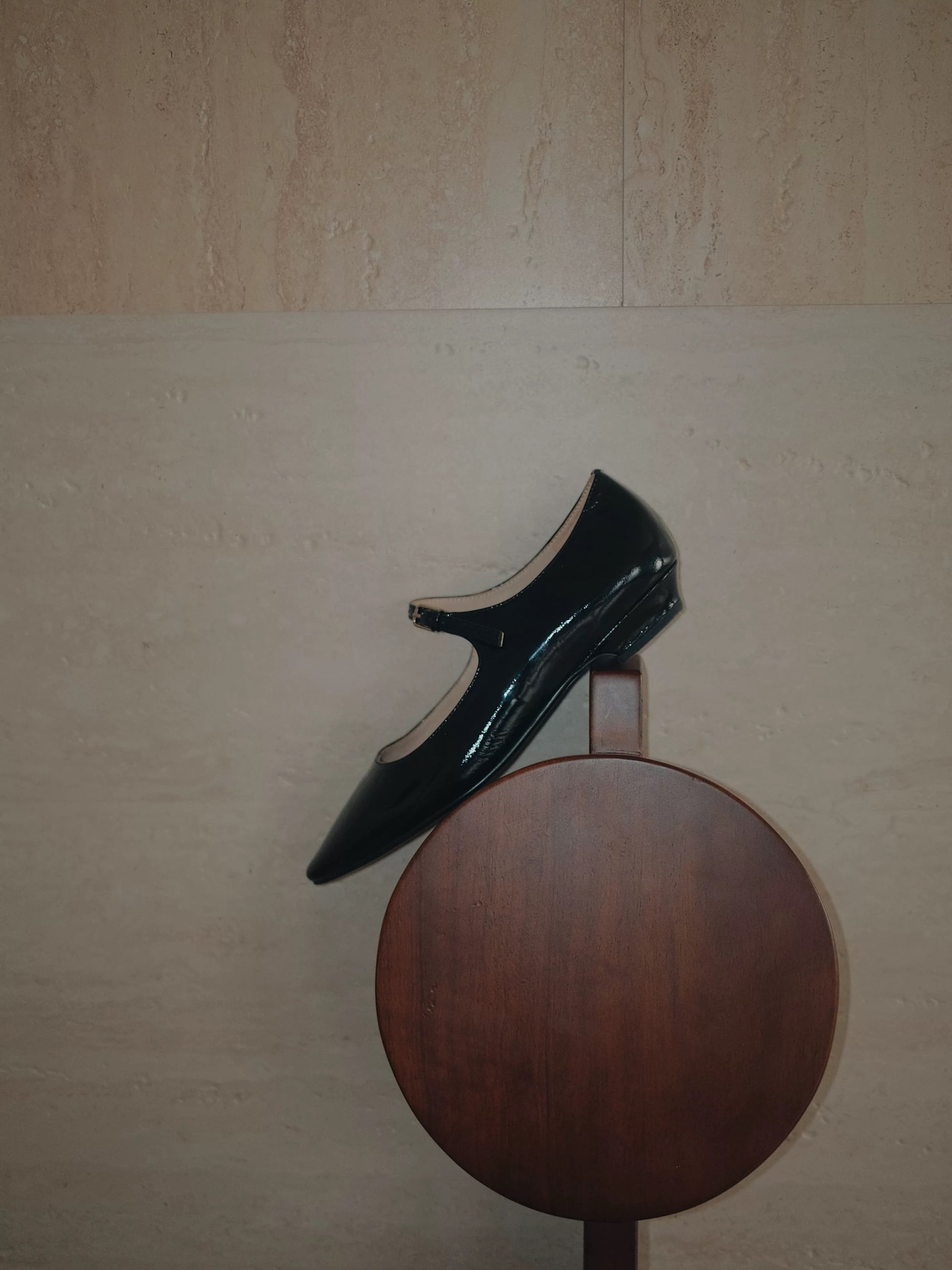 A balck patent leather pointed-toe Mary Jane flat shoe with a single strap, placed on a sculpture