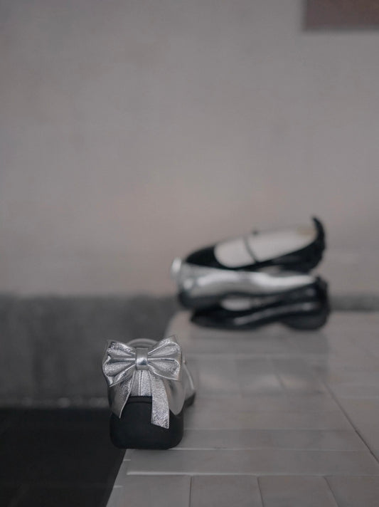 Showing three mary jane shoes stacked vertically in the back, and the back bow detail of the silver mary jane flats in the front
