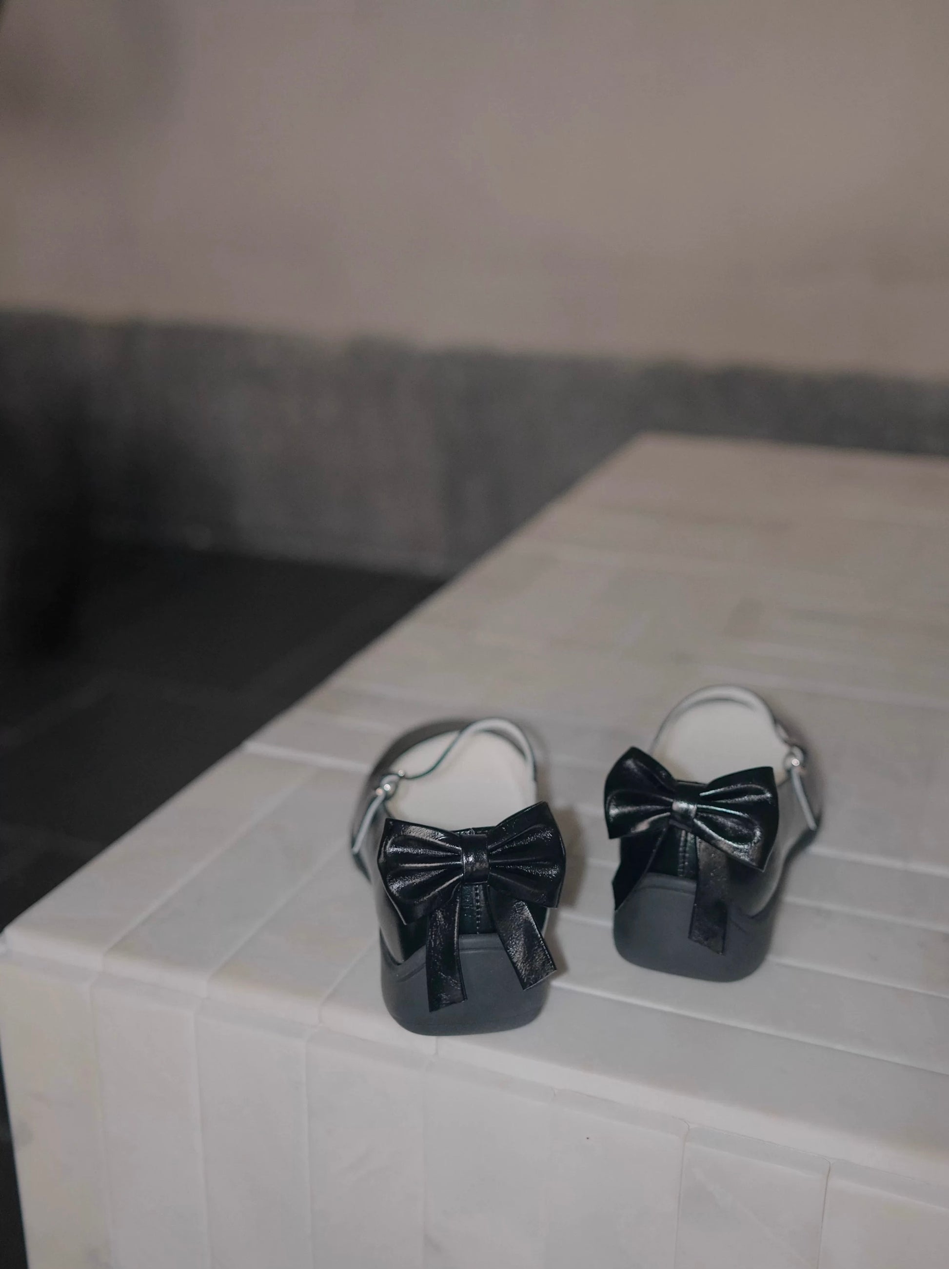 Sporty Mary Jane shoes in black with back bow place on a dark rought floor - back view - showing the bow details
