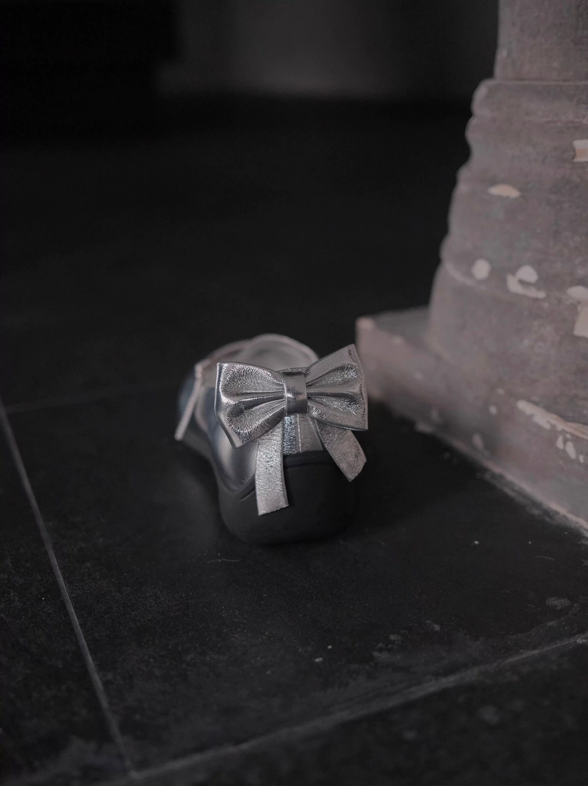 Sporty Mary Jane shoes in shimmering silver with back bow place on a dark rought floor - back view - showing the bow details