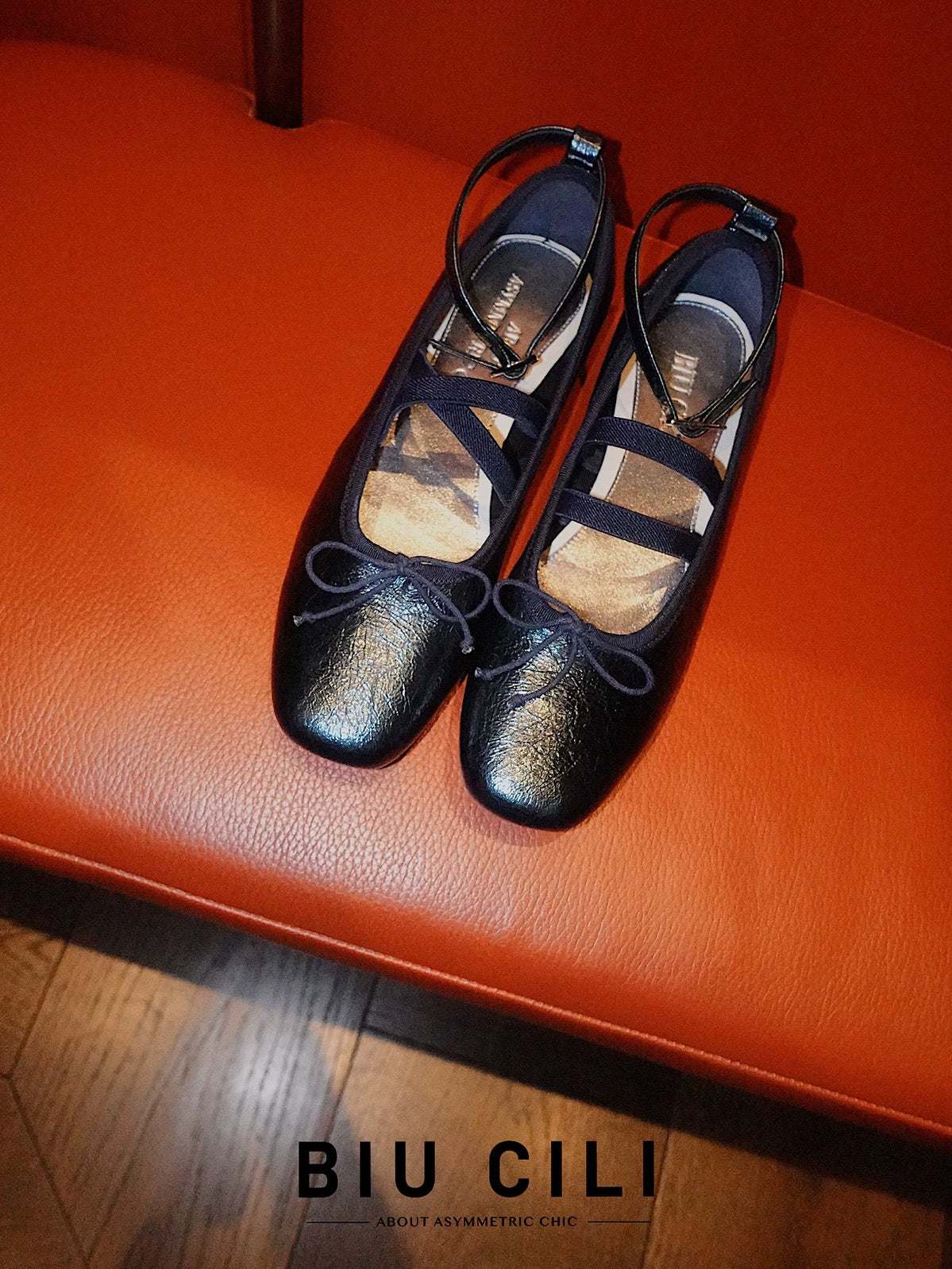 navy metallic leather Mary Jane ballet flats with asymmetrical cross straps placed on a orange leather surface
