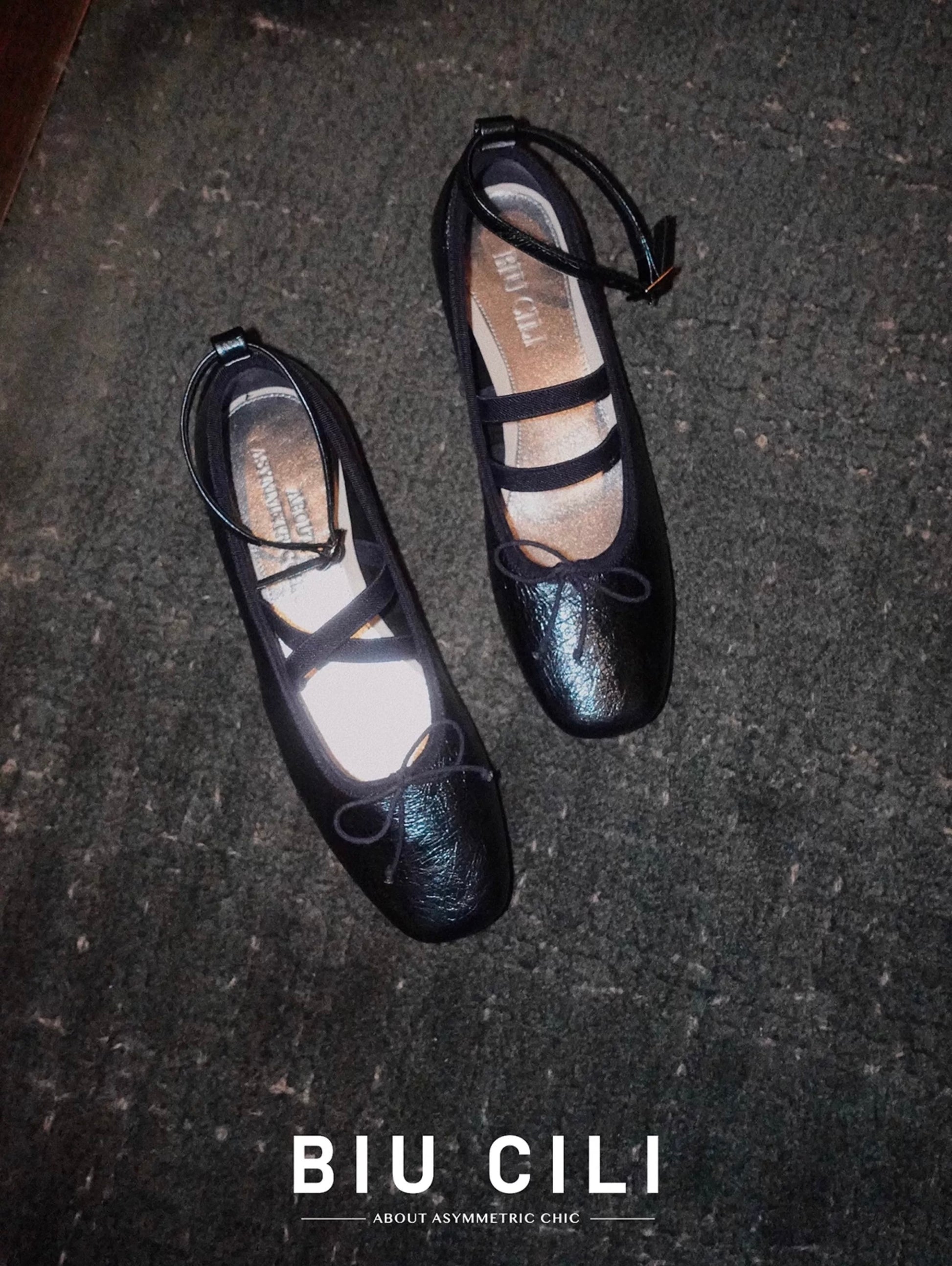 Top view of navy metallic leather Mary Jane ballet flats with asymmetrical cross straps under a chic dark light, placed on the carpet